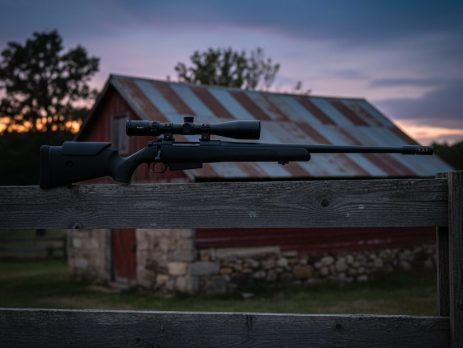 A compact scoped air rifle on a rest near a farm building.